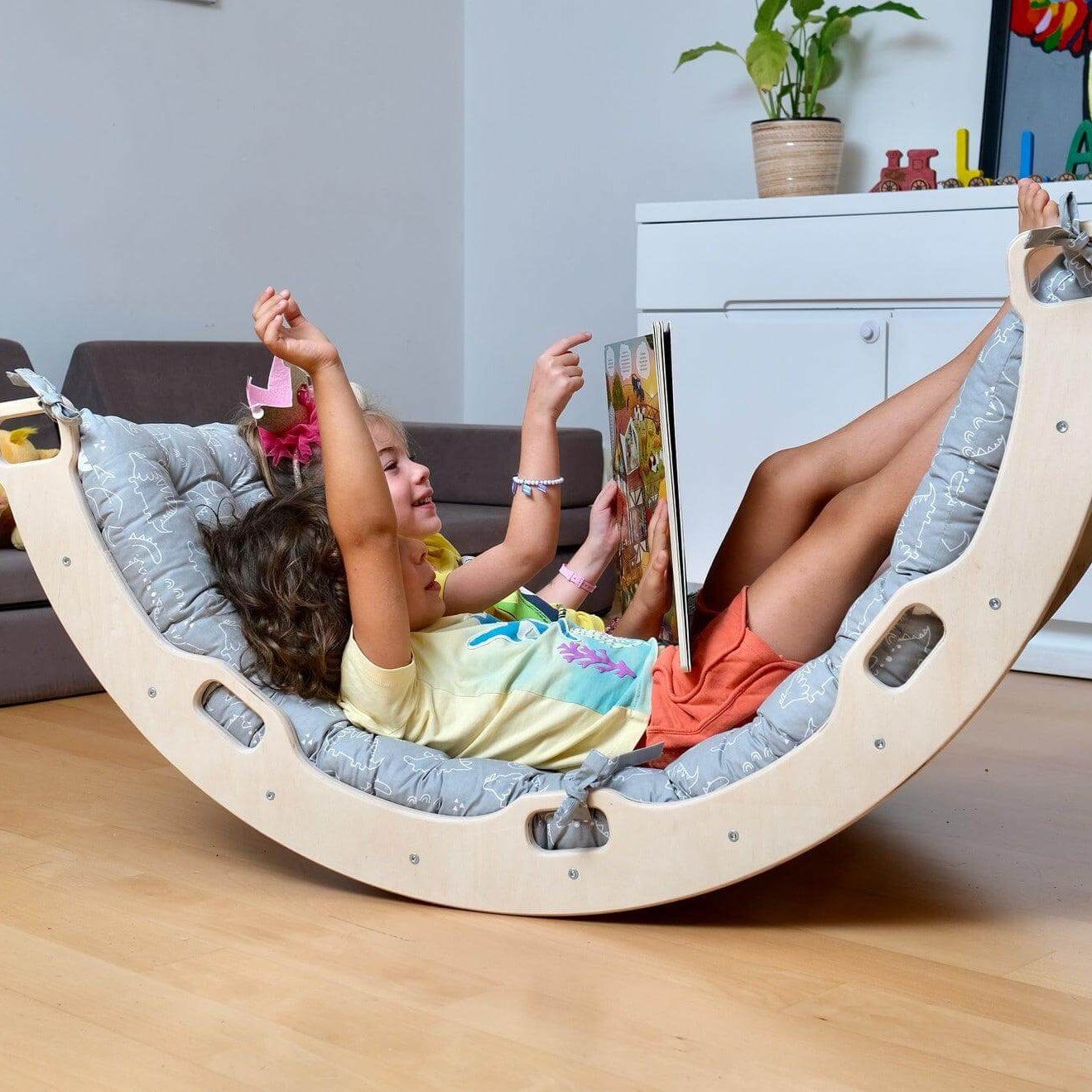 Child playing and reading on a Montessori Arch/Rocker with gray dinosaur pattern pillow in a living room setting