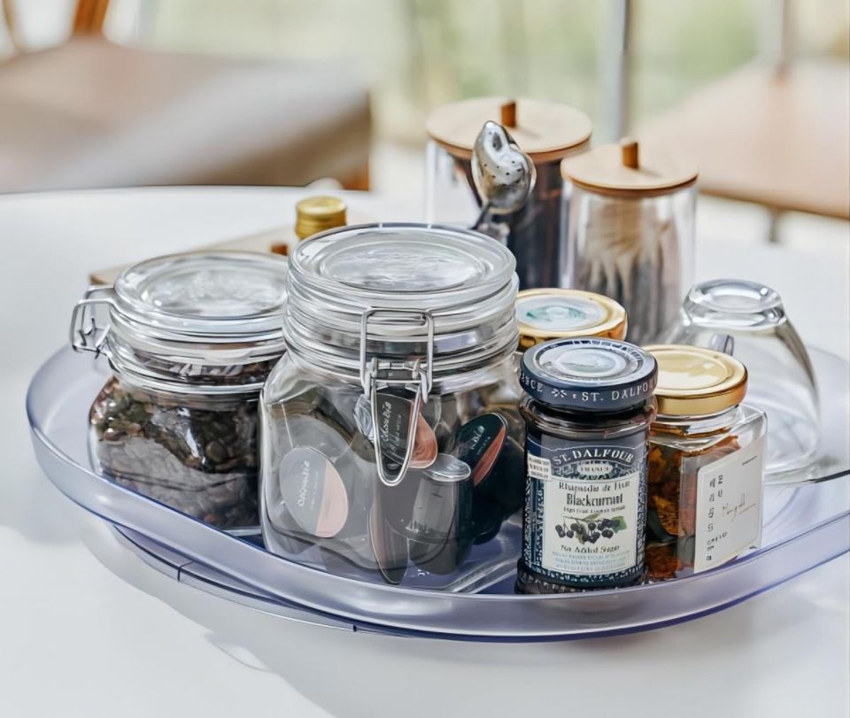 Clear rectangular Lazy Susan turntable organizer with sliding and 360° rotation, holding jars and containers on a kitchen table