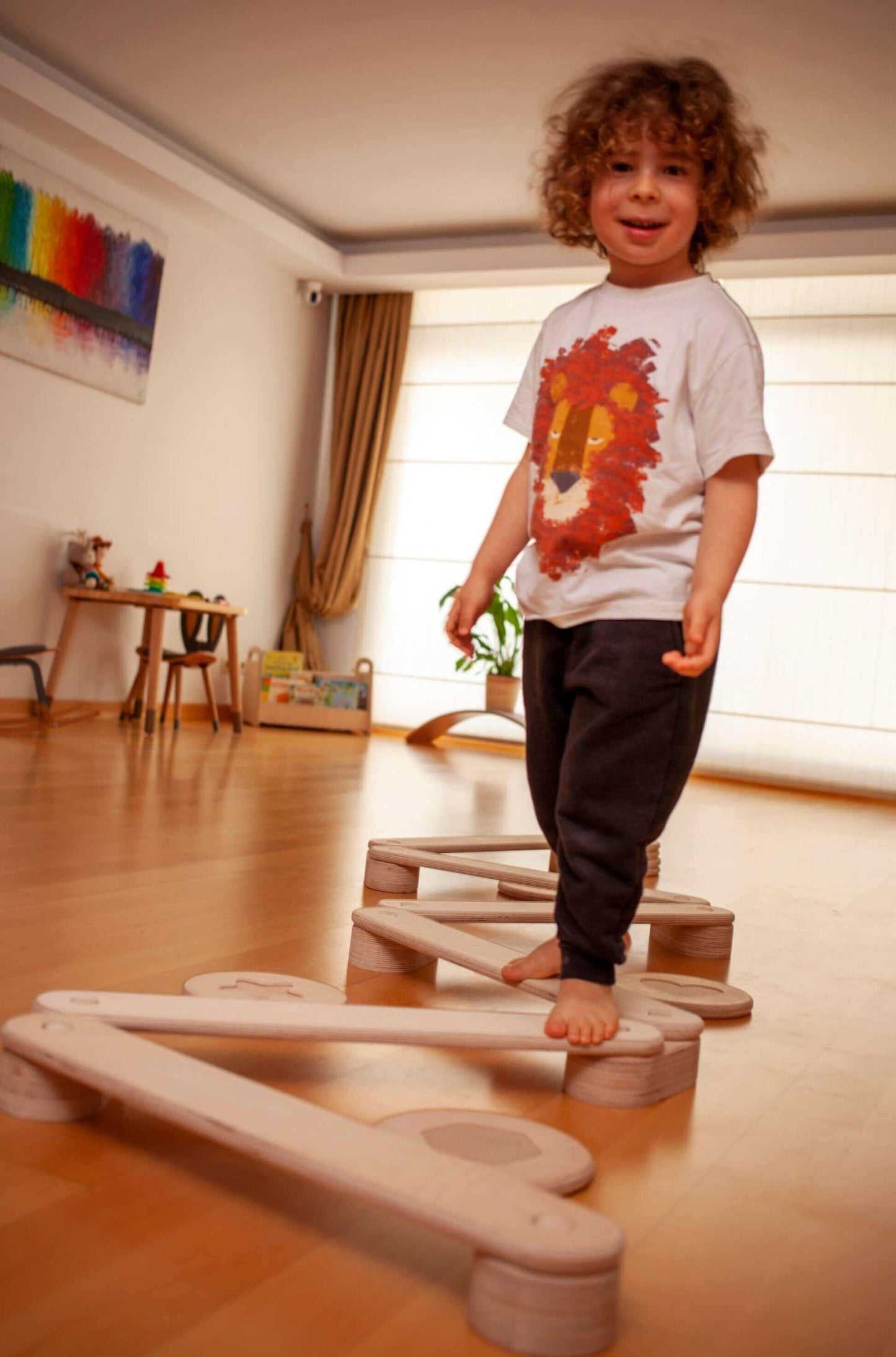 Child playing barefoot on Montessori wooden balance beam and stepping stones set indoors for motor skill development