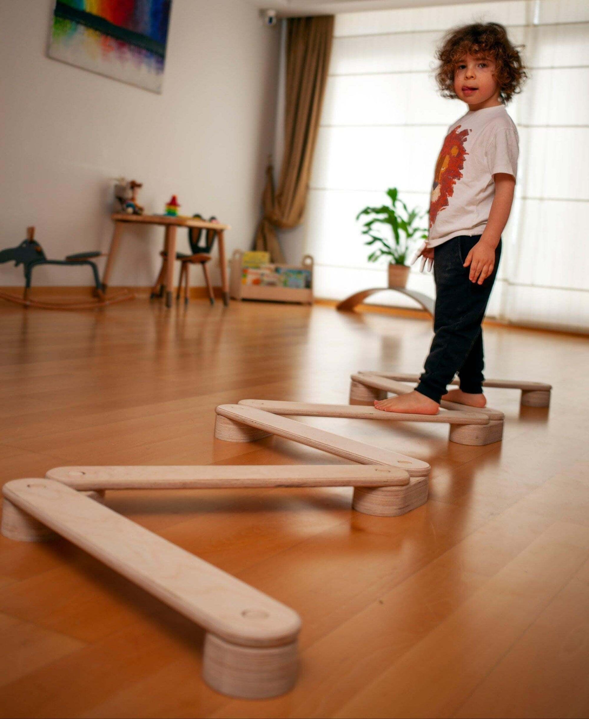 Toddler balancing on natural birch wood Montessori balance beam set in playroom for coordination and motor skills development