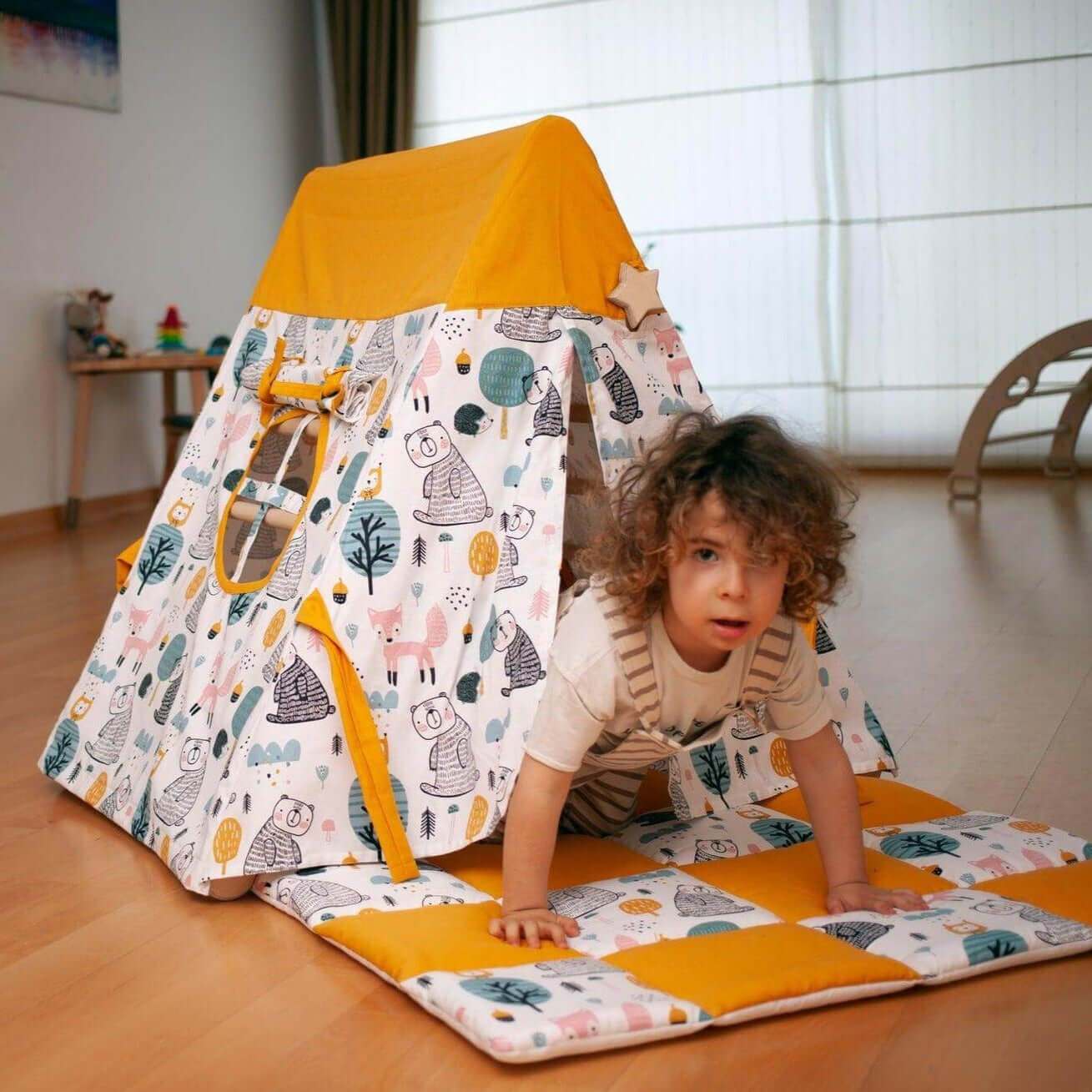 Toddler playing on foldable climbing triangle with colorful animal print tent cover and matching play mat indoors