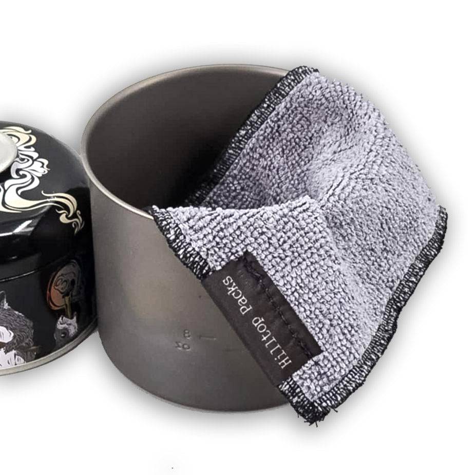 Gray microfiber pot cleaning rag draped over a metal cooking pot with a decorative lid nearby