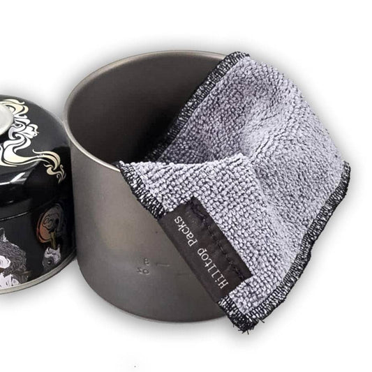Gray microfiber pot cleaning rag draped over a metal cooking pot with a decorative lid nearby