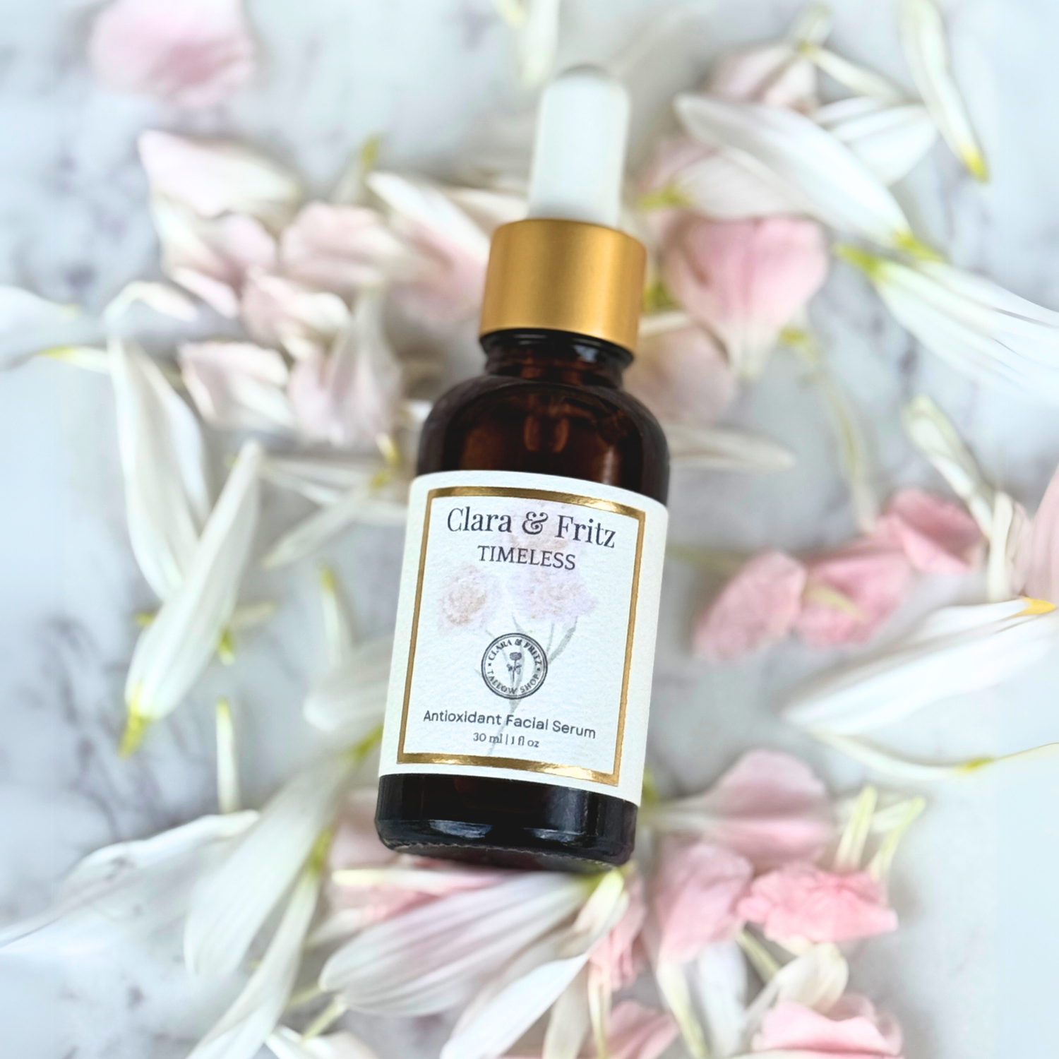 Brown glass dropper bottle of Timeless Antioxidant Facial Serum by Clara & Fritz surrounded by soft pink and white flower petals on a marble surface