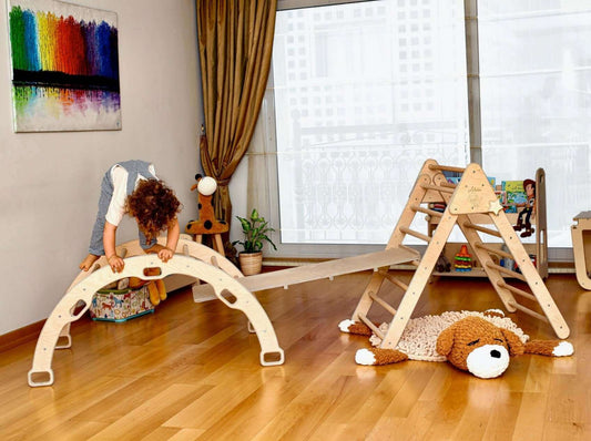 Child playing on a wooden foldable 4-piece climbing set including climbing triangle, arch rocker, pillow, and 2-in-1 ramp in a bright indoor room