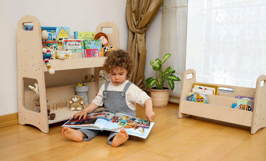 Child sitting on floor reading book next to small wooden bookshelf filled with colorful children's books and toys in a bright room