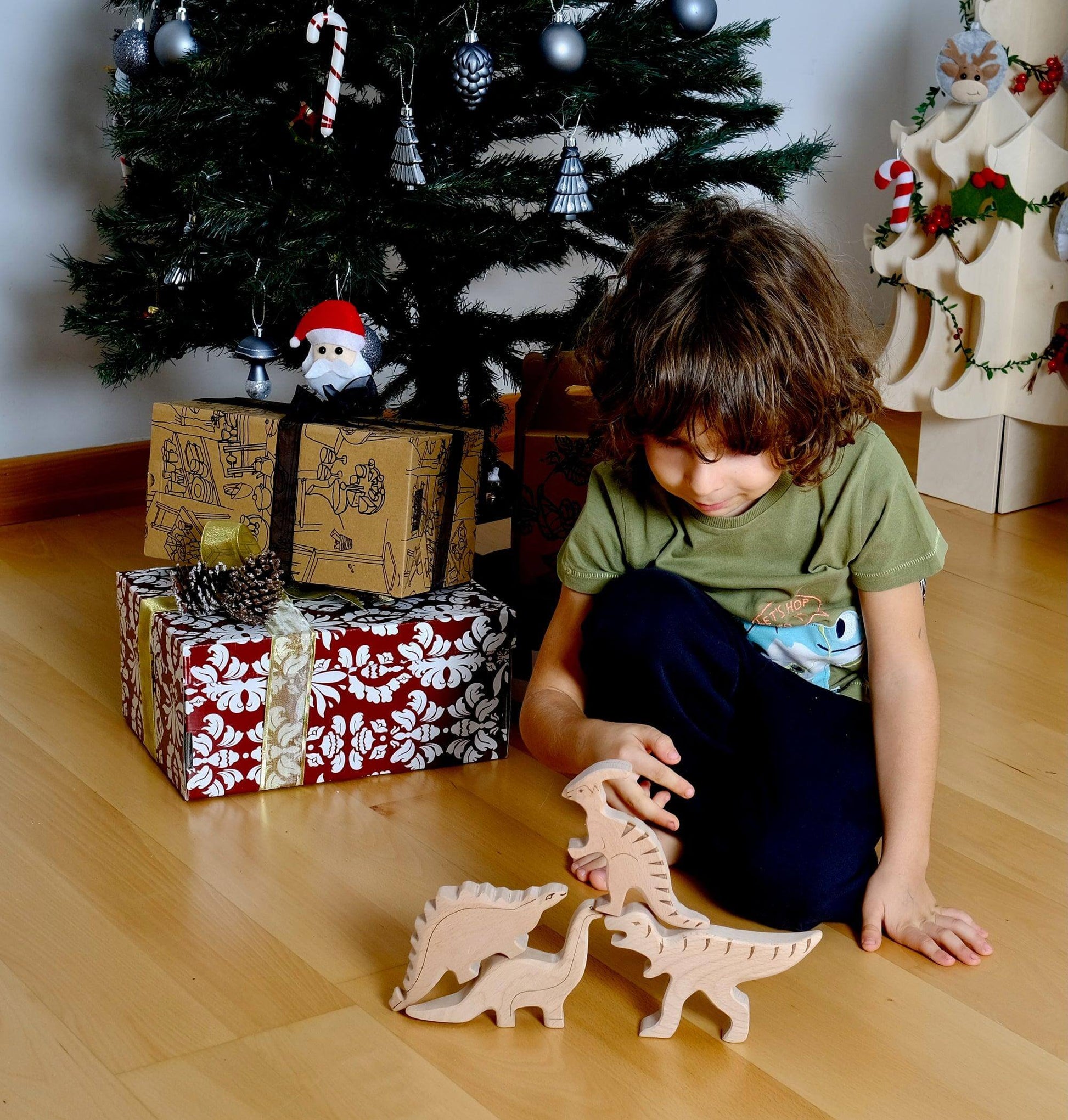 Child playing with handcrafted wooden dinosaur set toys on wooden floor near Christmas tree and wrapped presents