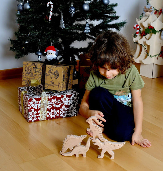 Child playing with handcrafted wooden dinosaur set toys on floor near Christmas tree and wrapped gifts