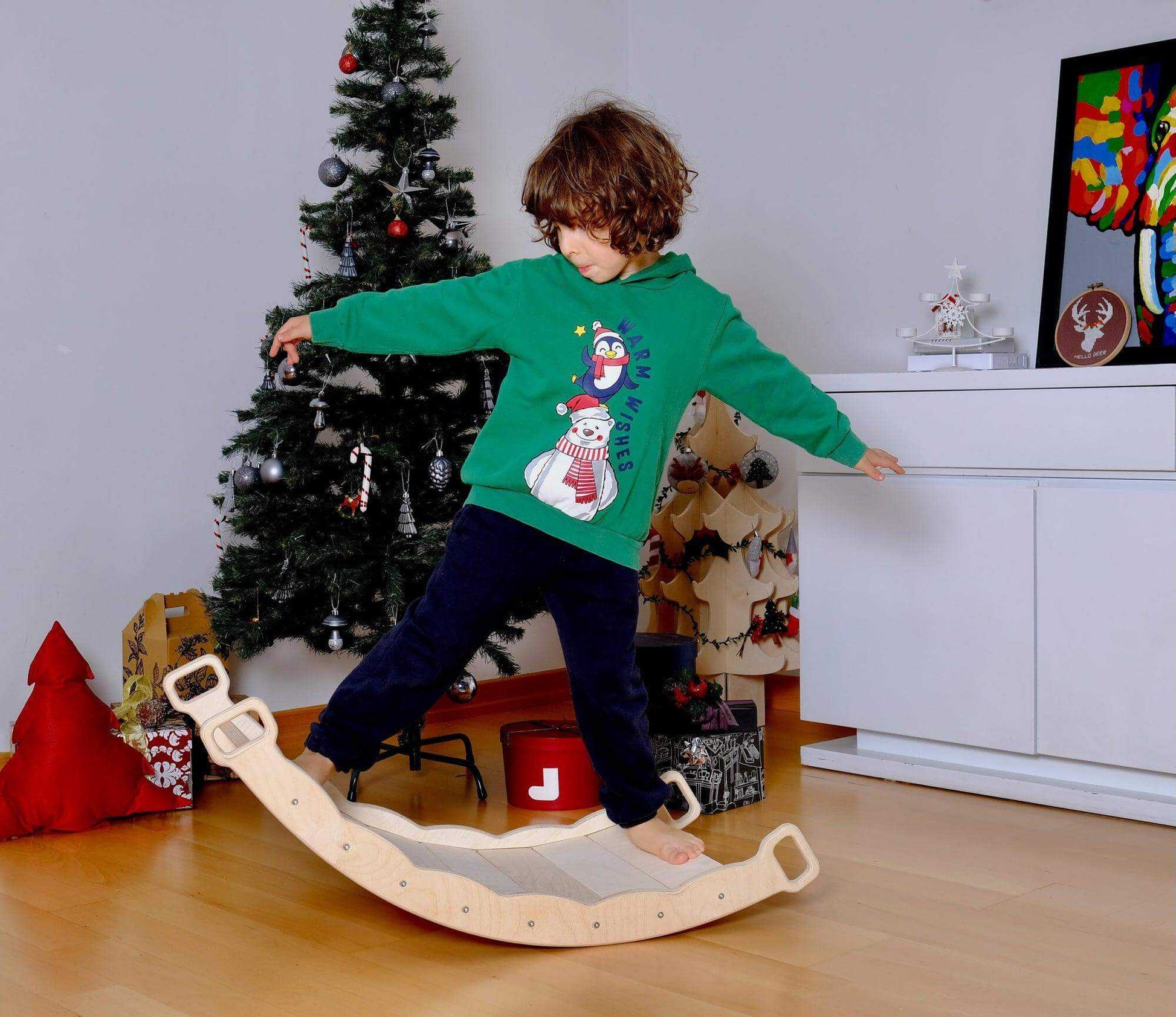 Child playing on XL wooden balance board with handles in festive room near Christmas tree