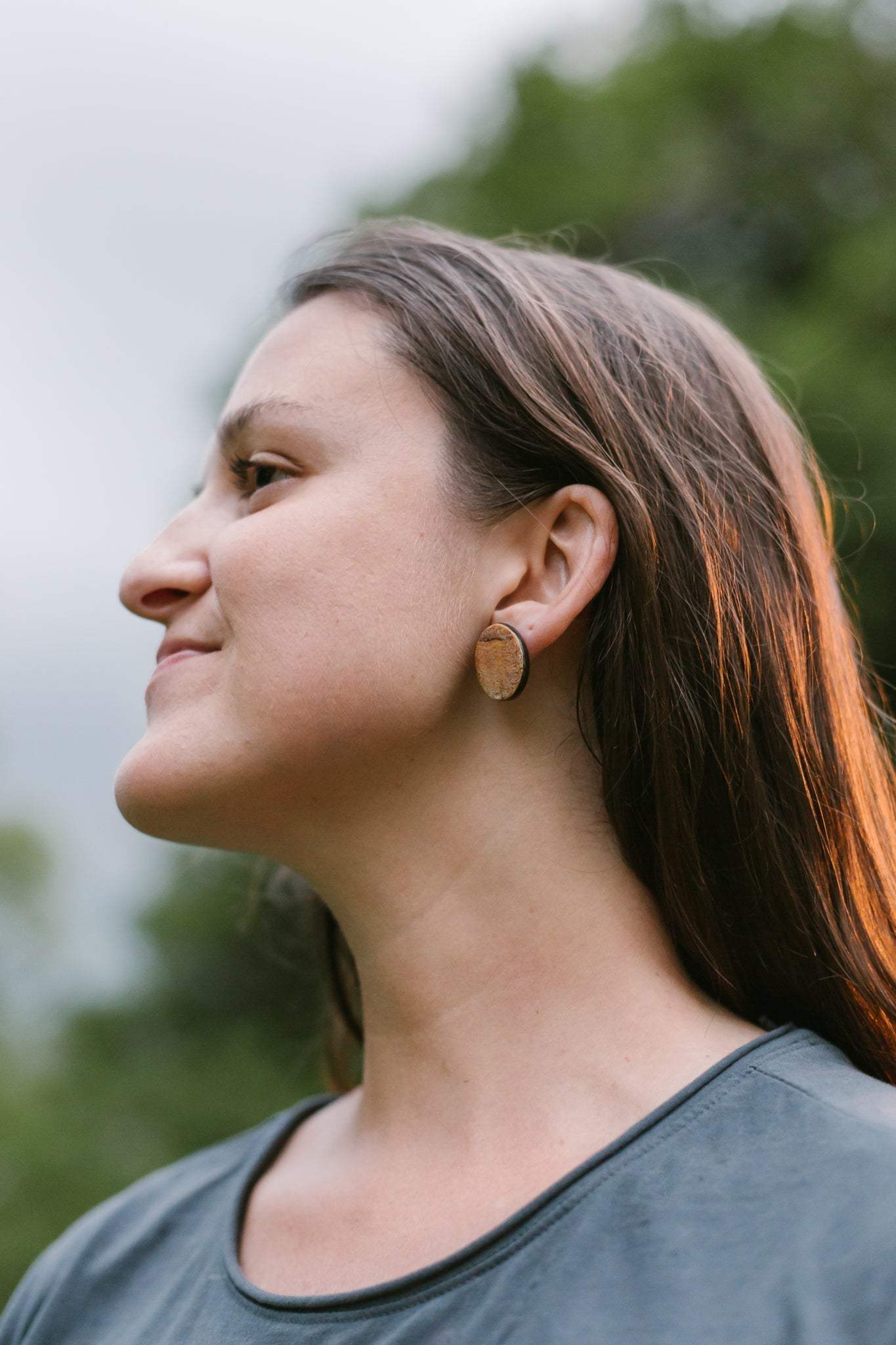 Woman wearing a minimalist horn stud earring made of gold plated brass and horn outdoors