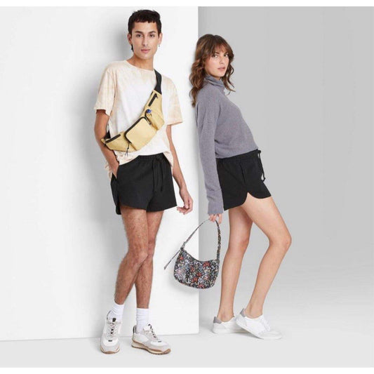 Man and woman wearing black high-rise dolphin shorts with casual tops and sneakers in a studio setting