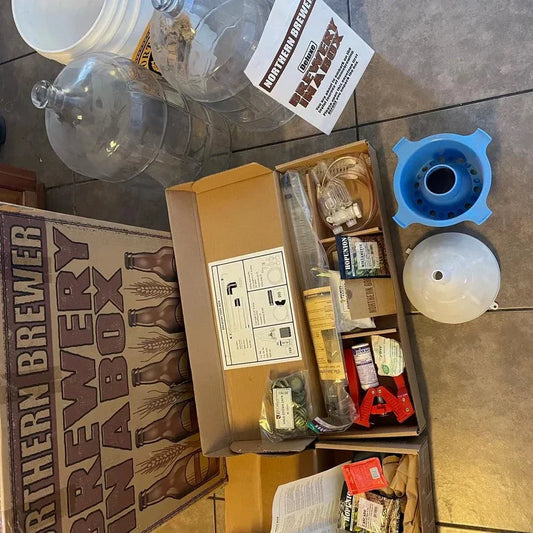 NORTHERN BREWER Deluxe Homebrew Starter Kit with unopened packaging and brewing accessories including glass carboys and fermentation bucket